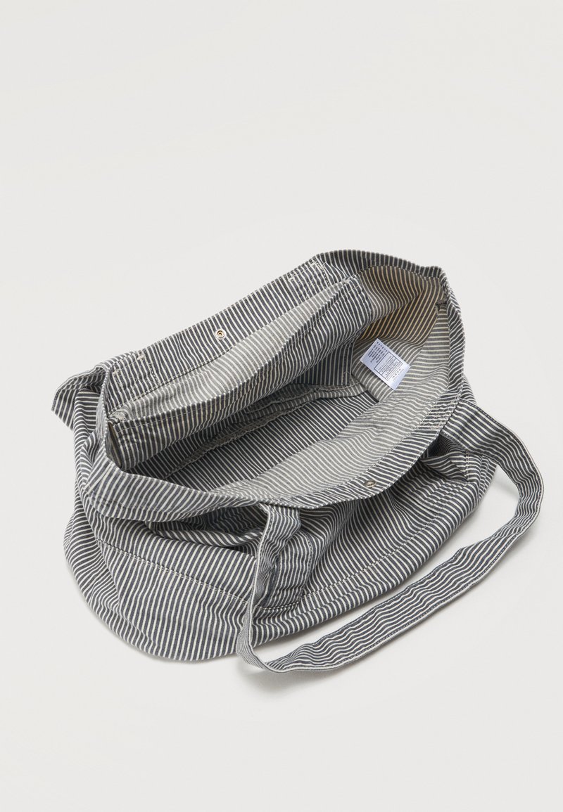 Sac fourre-tout en tissu rayé gris et blanc avec de longues poignées, ouverture supérieure et étiquette intérieure visible à l'intérieur du sac.