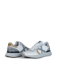 Scarpe sportive bianche con una combinazione di accenti grigi, beige e neri. Materiali in mesh testurizzato e pelle liscia con suola piatta.