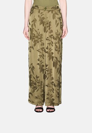 Pantaloni verde oliva a gamba larga con stampa a foglie scure indossati con sandali neri aperti sulle dita e top verde oliva, mostrati dalla vita in giù.