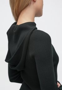 Pulover verde închis cu glugă, cu textură striată. Prezintă o croială relaxată și o glugă moale care cade frumos, evidențiind elasticitatea și căldura piesei vestimentare.