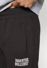 Crne trenirke od mješavine pamuka. Imaju elastičnu koricu, bočnu džepu i bijeli ispisani logo "JUVENTUS MILLE897".