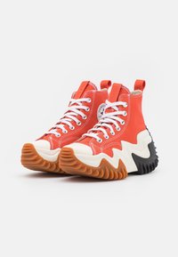 Sneakers alti rossi con lacci bianchi, suole in gomma e design a zigzag. Materiale in tela e patch con logo sul lato.