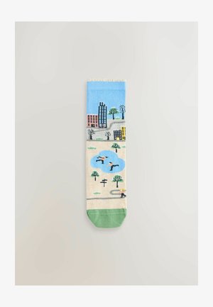 Chaussette montante présentant un ciel bleu et une scène urbaine avec des bâtiments, des arbres et des personnes. Corps crème avec des accents verts au niveau des orteils et de la cheville.