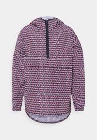 Bunter Kapuzenpullover mit einem Reißverschlusskragen und einem ganzflächigen geometrischen Muster in Rot, Weiß und Blau auf einem dunklen Hintergrund.