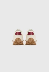 Sneakers con una toma bianca, accento a tacco color maroone e suola in gomma marrone con un motivo a spina di pesce. Design minimalista con una texture liscia.