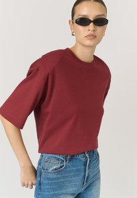 Burgundské oversized tričko vyrobené z m�ěkké bavlny s krátkým rukávem, spárované s modrými džínami s vysokým pasem. Jednoduchý kulatý výstřih.