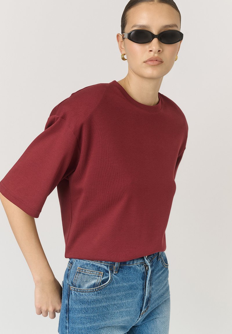 Burgundské oversized tričko vyrobené z měkké bavlny s krátkým rukávem, spárované s modrými džínami s vysokým pasem. Jednoduchý kulatý výstřih.