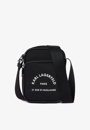 Černá krosová taška vyrobená z nylonu. Má obdélníkový tvar, výrazné bílé logo vpředu a nastavitelný popruh.