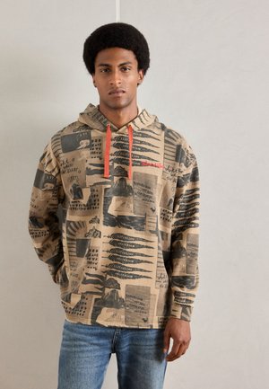 Felpa marrone con stampe grafiche in nero e rosso. Presenta un cappuccio con cordini e una vestibilità rilassata. Abbinata a jeans blu.