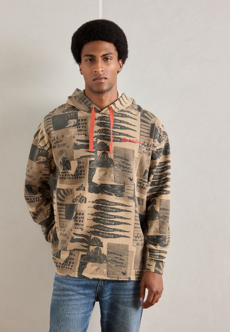 Brown hoodie with graphic prints in black and red. Features a drawstring hood and a relaxed fit. Paired with blue jeans.