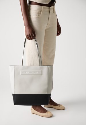 Sac fourre-tout gris et noir avec un design structuré, fabriqué dans un matériau lisse, avec une marque visible sur une patch rectangulaire.