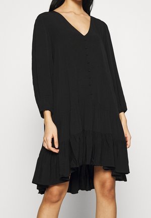 Robe noire à col en V, manches longues, fermeture à boutons sur le devant et ourlet à volants. Fabriquée en tissu léger et texturé.