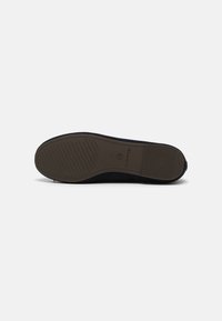 Semelle d'une chaussure noire montrant un motif antidérapant, taille 37 et nom de la marque Tamaris sur fond blanc uni.