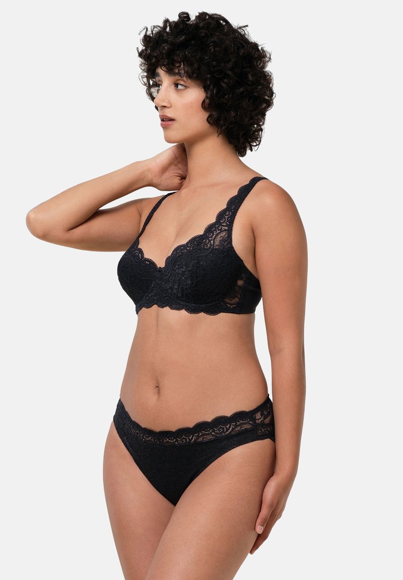 Svart spets-bh med vågiga kanter och matchande spetsbikini. Har genomskinliga paneler och texturerade blommönster i hela designen.