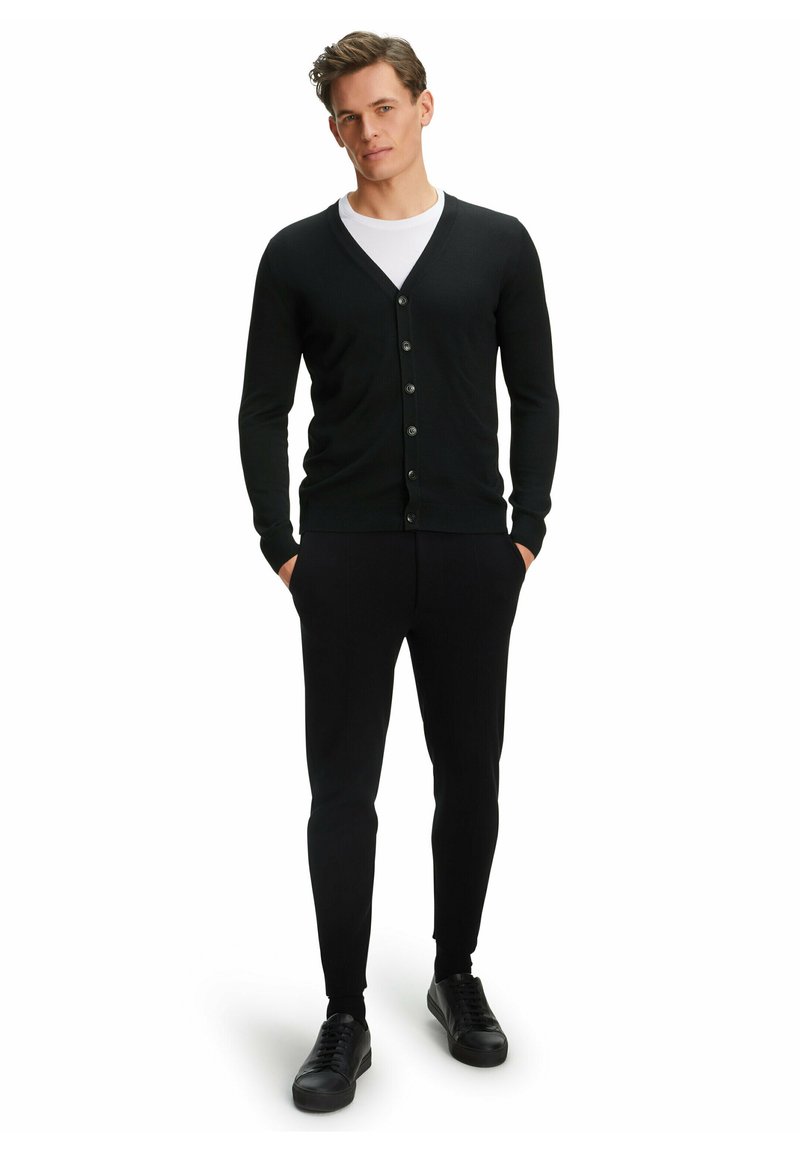Cardigan nero con scollatura a V, chiusura con sei bottoni, texture a coste, abbinato a pantaloni neri slim-fit e sneakers nere.