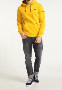 Žlutá mikina s klokanní kapsou, stahovacími šňůrkami a logem. Vybaveno šedými džíny a námořnickými teniskami. Jednoduchá textura, ležérní design.