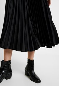 Svart plisserad kjol med en flödande design och mjuk textur, i kombination med svarta anklarstövlar med en glänsande, krokodilmönstring.