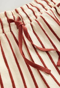 Gestreepte, crèmekleurige katoenen shorts met bordeaux verticale lijnen, voorzien van een elastische tailleband en een bijpassende strik. Zachte textuur, casual ontwerp.