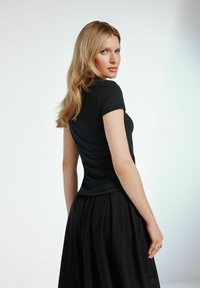 Czarny dopasowany top z krótkim rękawem o gładkiej teksturze, zestawiony z zwiewną czarną spódnicą. Top ma okrągły dekolt i minimalistyczny design.