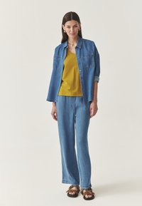 Denimist särk, kollane topp, laiad sinised teksapüksid ja pruunid sandaalid. Särgil on kaks rinnataskut, rullitud varrukad; pehme kangas, lõdvestunud lõige.