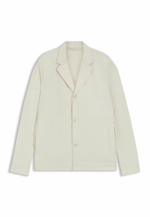 Veste beige clair avec un col cranté, fermeture à bouton et zips latéraux. Fabriquée en tissu lisse et texturé avec une coupe ajustée.