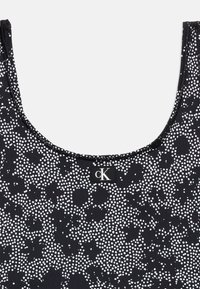 Μαύρο αμάνικο τοπ με λευκό πουά λουλουδάτο σχέδιο και μικρή ετικέτα με το λογότυπο cK στο κέντρο κοντά στη λαιμόκοψη.