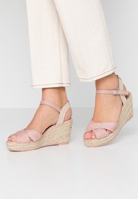Růžové klínové sandály s kříženými popruhy, espadrilkovým provázkovým detailem na pevné korkové podrážce, s nastavitelnými kotníkovými pásky a hladkým povrchem.