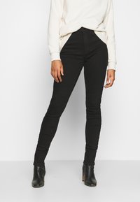 Svarta skinny jeans med hög midja, tillverkade av elastisk denim, kombinerade med en ljusgräddasweater och svarta klackstövlar.