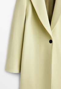 Manteau en laine jaune clair avec col châle, fermeture à un bouton, et manches larges. Présente une texture lisse avec une finition douce.