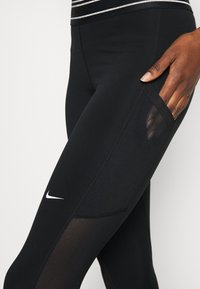 Svarta leggings med en slät yta, med ett sidopanel i mesh, kontrasterande sömmar och en liten vit logotyp på låret.