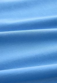 Helles blaues Baumwollgewebe mit glatter Textur, das feine Rippungen und Falten aufweist, die Tiefe und Schatteneffekte erzeugen.
