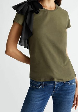 Olive zielona bluzka z krótkim rękawem, z czarnym szyfonowym falbanką na lewym ramieniu, gładka w dotyku, z okrągłym dekoltem.