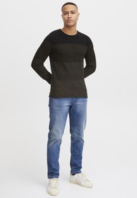 Knit sweater in dark green with black textured upper portion. Paired with blue denim jeans and white sneakers. Long sleeves and crew neck design.