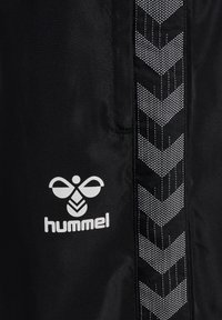 Schwarze Sportshorts aus Stoff mit einem weißen "hummel"-Logo und einem kontrastierenden Chevron-Muster an der Seite in Grau und Weiß.