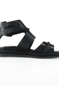 Sandale en cuir noir avec double sangle ajustable à la cheville, détail tressé sur la lanière des orteils et semelle plate rembourrée.