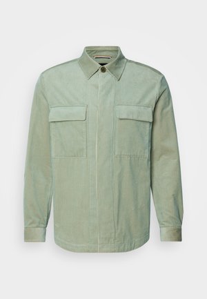 Šviesiai žalias kordūrinis marškinis su vertikaliomis juostelėmis, turintis smailų apykaklę, dvi krūtinės kišenes ir mygtukų užsegimą. Ilgos rankovės su rankogalių detalėmis.