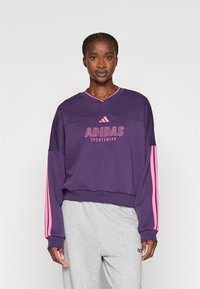 Sudadera morada con rayas rosas en las mangas, que presenta el logo "ADIDAS SPORTSWEAR" en rosa en la parte frontal. Tejido ligero.