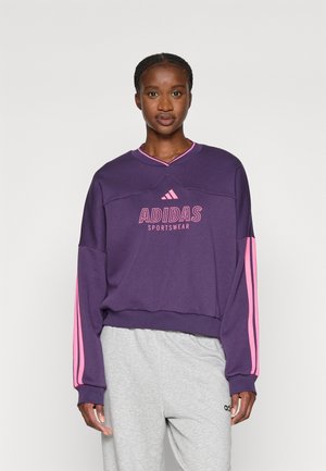 Sudadera morada con rayas rosas en las mangas, que presenta el logo "ADIDAS SPORTSWEAR" en rosa en la parte frontal. Tejido ligero.
