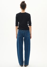 Černý žebrovaný top s krátkým rukávem, který je spárován s vysokými modrými širokými džíny. Džíny mají klasický pětivreckový design a denimovou texturu.