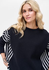 Czarny sweter z białymi pionowymi paskami na rękawach, okrągłym dekoltem i miękką fakturą. Dodatki obejmują luźny krój.
