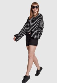 Black and white striped oversized sweater, loose sleeves, paired with black shorts and black shoes. Model wearing dark sunglasses.