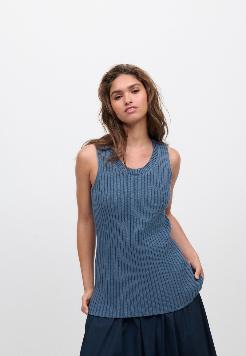 Top sin mangas acanalado en tejido de punto azul suave, con cuello redondo y dobladillo ligeramente curvado, combinado con una falda oscura.