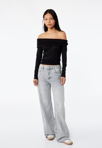 Top lungo nero off-the-shoulder con maniche lunghe abbinato a jeans larghi grigio chiaro, caratterizzato da una vestibilità comoda e una leggera texture sfumata.