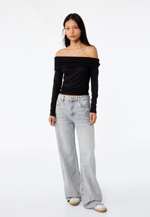 Schwarzes, schulterfreies Oberteil mit langen Ärmeln, kombiniert mit hellgrauen weit geschnittenen Jeans, die einen entspannten Schnitt und eine dezente, ausgebleichte Textur aufweisen.