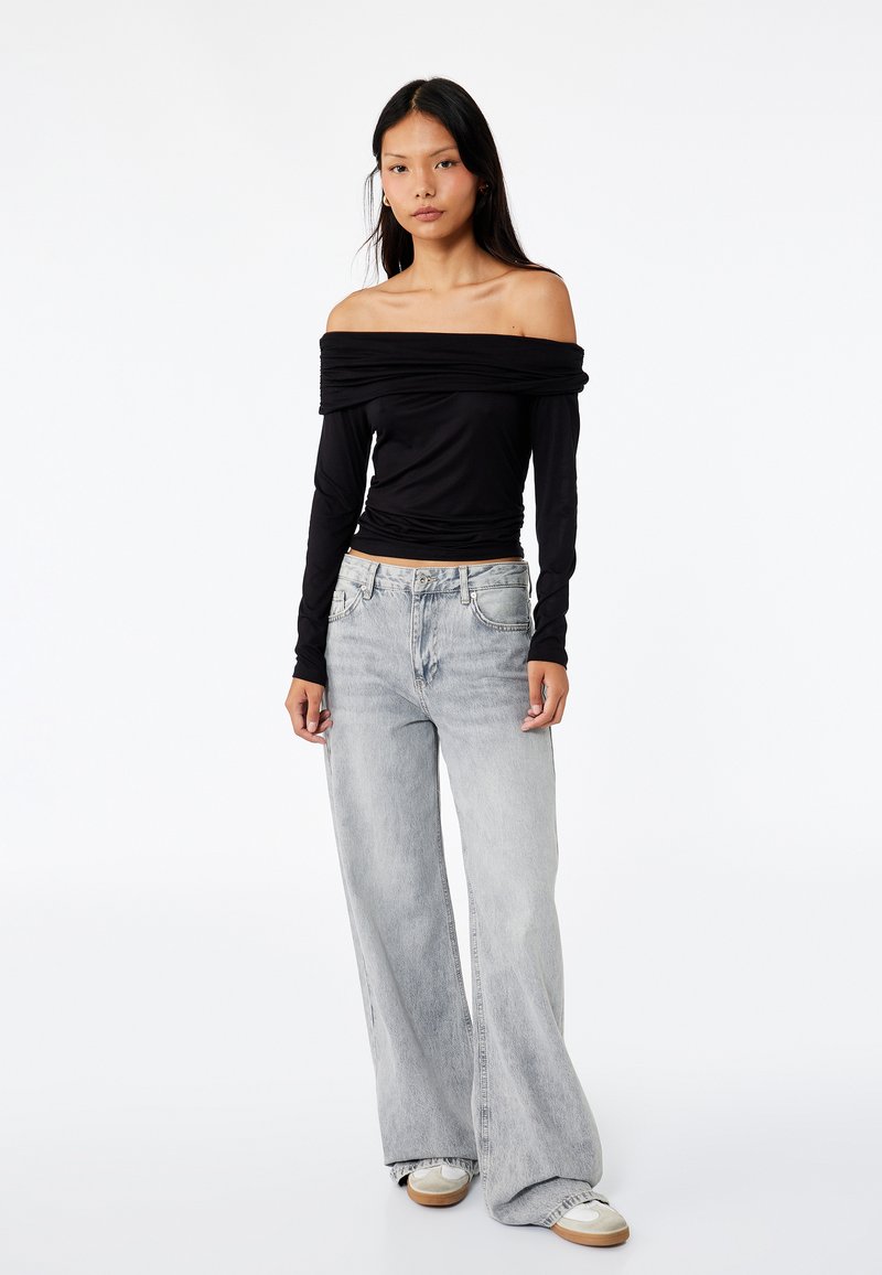 Top lungo nero off-the-shoulder con maniche lunghe abbinato a jeans larghi grigio chiaro, caratterizzato da una vestibilità comoda e una leggera texture sfumata.