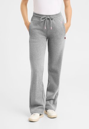 Person wearing grey drawstring sweatpants and white sneakers standing with hands in pockets on a plain background.