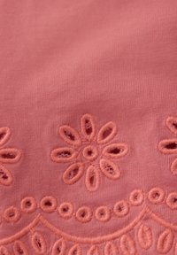Bomullstyg i mjuk laxrosa med blommönsterbroderi. Har öppet arbete och texturerade detaljer längs kanterna.