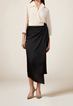 White long-sleeve blouse with a wrap design, paired with a black satin asymmetrical skirt. Accented with snake print heels.