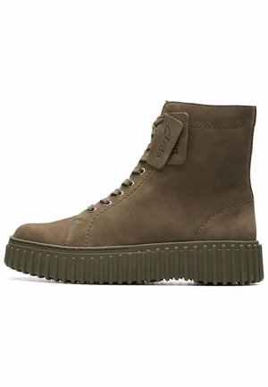 Brown suede ankle boots with a thick, ridged green rubber sole and classic lace-up design. Features a stitched tag on the collar.
