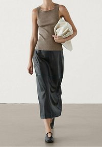 Brown ribbed tank top, black leather maxi skirt with front seam details, and black flat shoes. Model holding a white clutch.